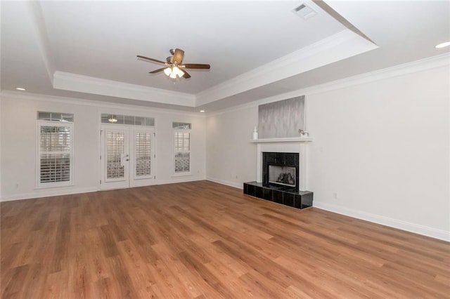 unfurnished living room featuring a tiled fireplace, visible vents, light wood finished floors, and a raised ceiling