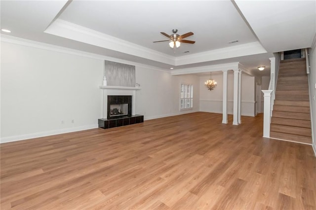 unfurnished living room featuring a tray ceiling, stairway, light wood-style flooring, and a tile fireplace