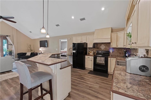 kitchen with black appliances, pendant lighting, vaulted ceiling, custom exhaust hood, and a kitchen bar