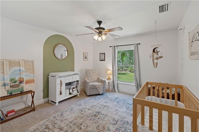 carpeted bedroom with a crib and ceiling fan