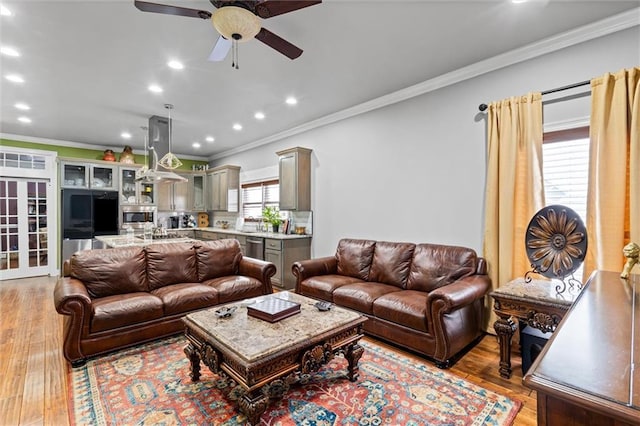 living room with ornamental molding, ceiling fan, and light wood-type flooring