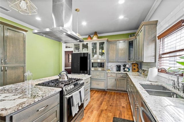 kitchen with appliances with stainless steel finishes, decorative light fixtures, island exhaust hood, ornamental molding, and light stone counters