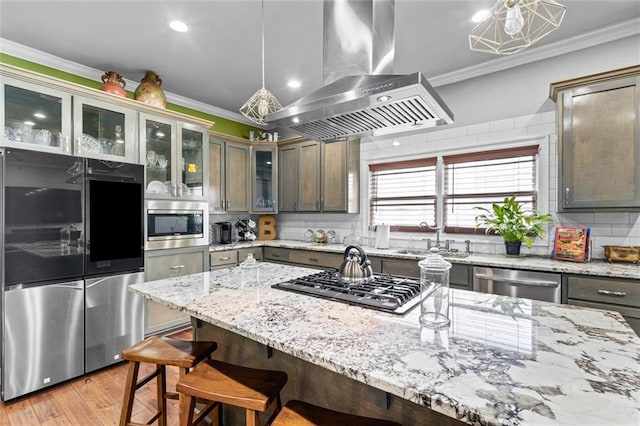 kitchen featuring sink, island range hood, appliances with stainless steel finishes, ornamental molding, and pendant lighting