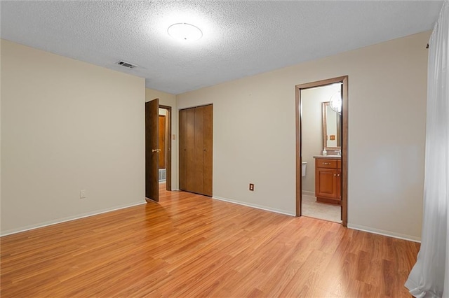 unfurnished bedroom with ensuite bathroom, a closet, a textured ceiling, and light hardwood / wood-style flooring