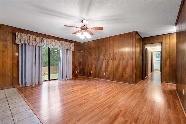 spare room with a textured ceiling, light hardwood / wood-style flooring, ceiling fan, and wood walls