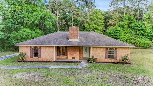 ranch-style home featuring fence, a shingled roof, brick siding, a front yard, and a chimney