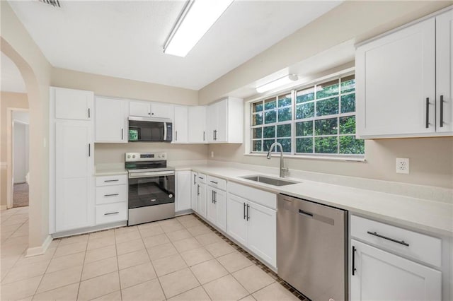 kitchen featuring white cabinets, appliances with stainless steel finishes, a sink, light countertops, and arched walkways