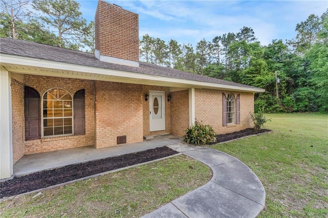 view of front of property featuring brick siding, a chimney, a shingled roof, and a front yard