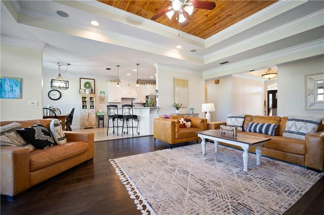 living room featuring ornamental molding, a tray ceiling, ceiling fan, and dark wood-type flooring