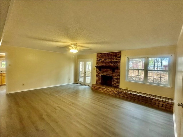 unfurnished living room with french doors, a textured ceiling, a brick fireplace, hardwood / wood-style flooring, and ceiling fan