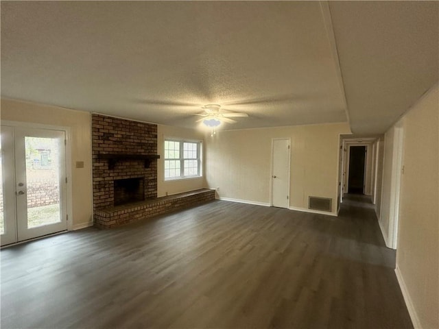 unfurnished living room featuring ceiling fan, a brick fireplace, dark wood-type flooring, and a textured ceiling