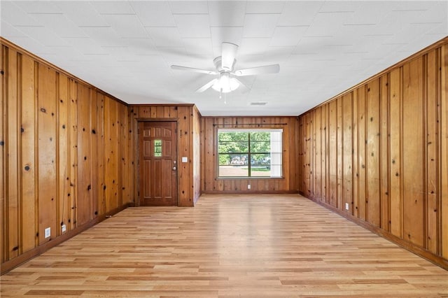 empty room featuring ceiling fan, wooden walls, and light wood-type flooring