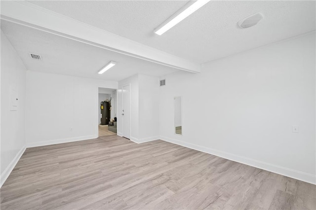 unfurnished room with beam ceiling, electric water heater, a textured ceiling, and light hardwood / wood-style flooring