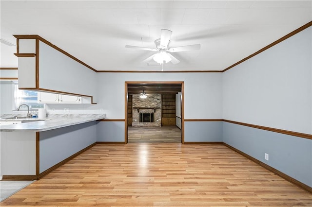 kitchen featuring a brick fireplace, ceiling fan, sink, light hardwood / wood-style floors, and white cabinetry