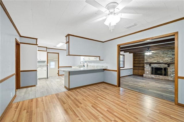 kitchen with a brick fireplace, kitchen peninsula, crown molding, white cabinets, and light wood-type flooring