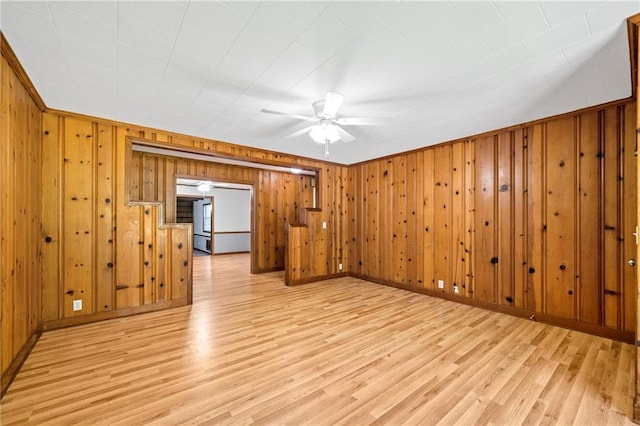 empty room featuring light hardwood / wood-style flooring, ceiling fan, and wood walls