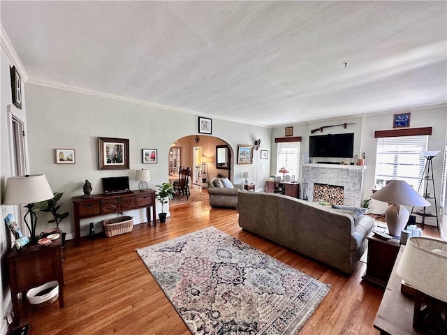 living room with a fireplace, wood-type flooring, a textured ceiling, and ornamental molding