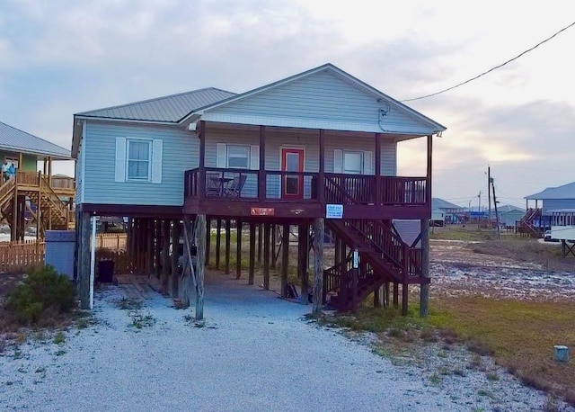 view of front of house with driveway, a carport, covered porch, metal roof, and stairs