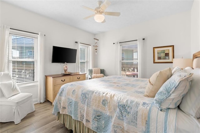 bedroom featuring light wood finished floors, a ceiling fan, baseboards, and multiple windows