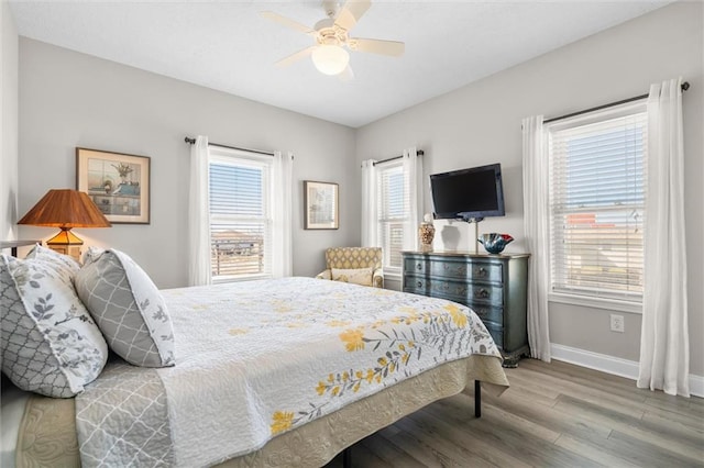 bedroom with baseboards, a ceiling fan, wood finished floors, and multiple windows