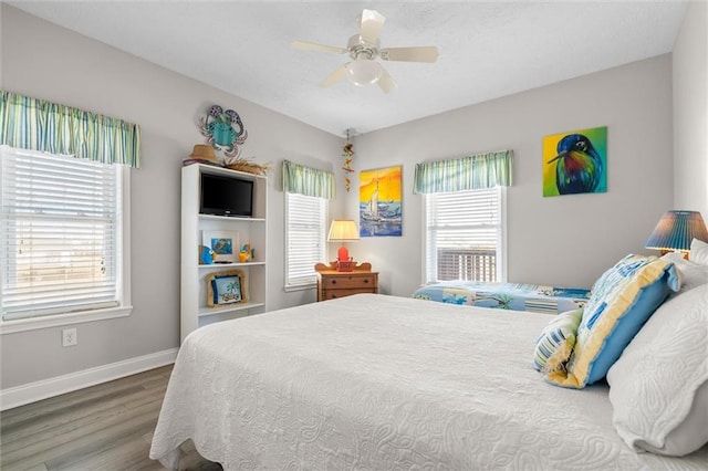bedroom featuring baseboards, a ceiling fan, wood finished floors, and multiple windows