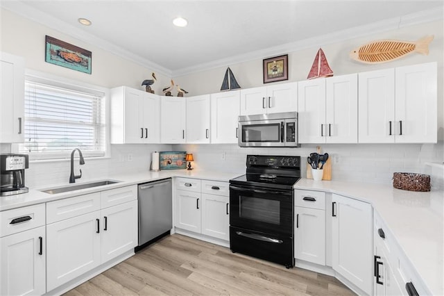 kitchen featuring white cabinets, stainless steel appliances, a sink, crown molding, and decorative backsplash