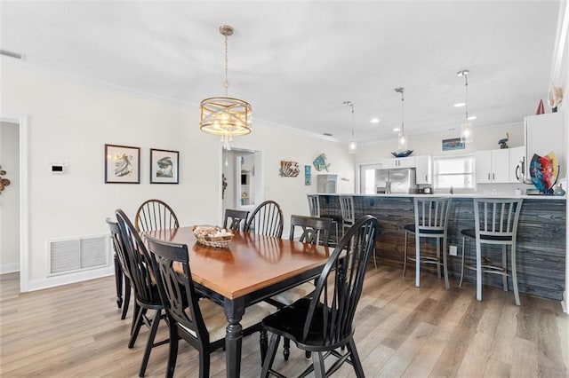 dining area with a chandelier, light wood-style floors, visible vents, and crown molding