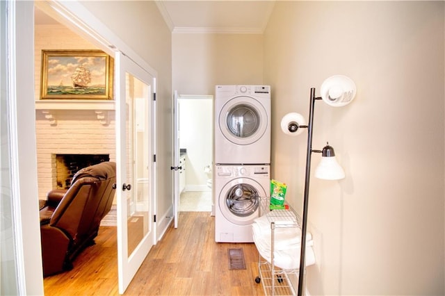 211 Cedar St, Mobile, AL 36602 - washroom featuring stacked washer / dryer, french doors, light wood-style floors, ornamental molding, and a fireplace