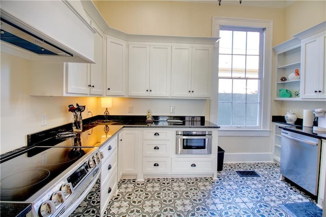 211 Cedar St, Mobile, AL 36602 - kitchen with appliances with stainless steel finishes, exhaust hood, white cabinetry, dark countertops, and open shelves