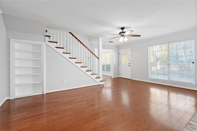 unfurnished living room with built in shelves, a textured ceiling, ceiling fan, and wood finished floors