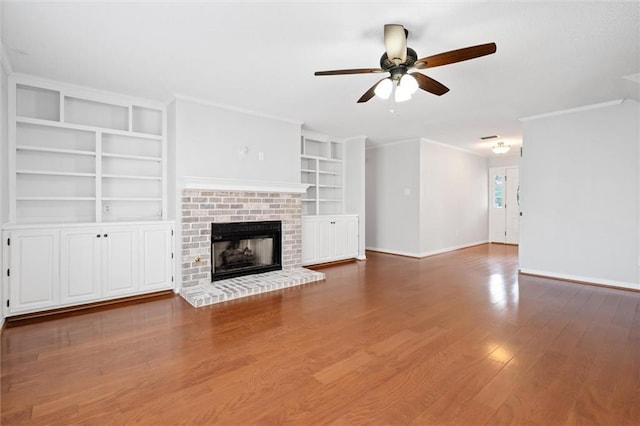 unfurnished living room with built in shelves, wood finished floors, baseboards, ornamental molding, and ceiling fan