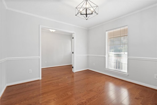 unfurnished room with a notable chandelier, crown molding, baseboards, and wood finished floors