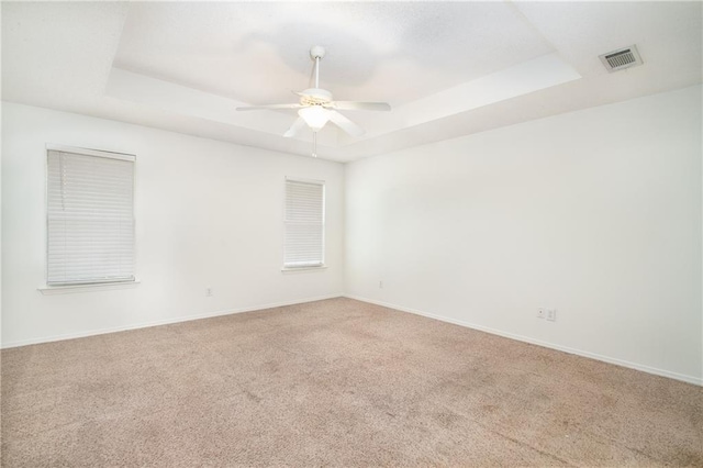 carpeted empty room with visible vents, a raised ceiling, ceiling fan, and baseboards