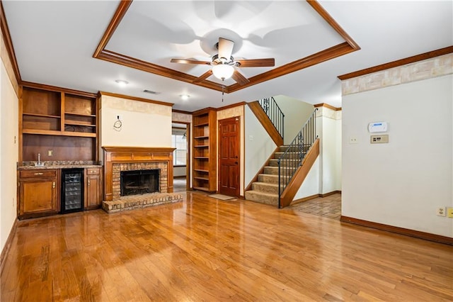 unfurnished living room with a tray ceiling, visible vents, crown molding, and stairway