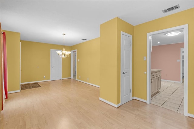 spare room featuring a notable chandelier, visible vents, and light wood-style flooring