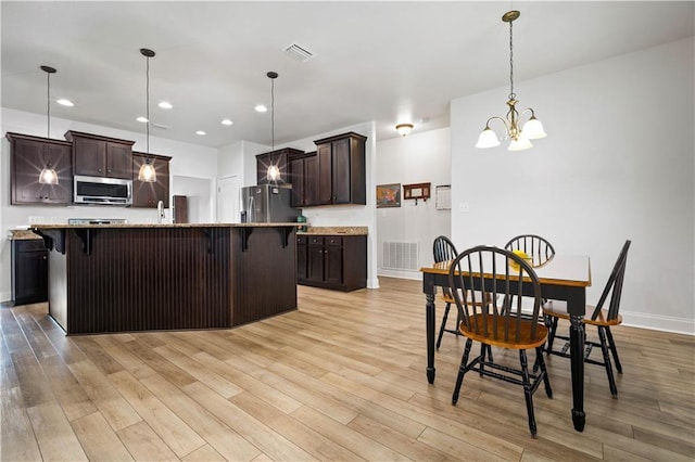 kitchen with visible vents, light wood finished floors, a breakfast bar, dark brown cabinets, and appliances with stainless steel finishes