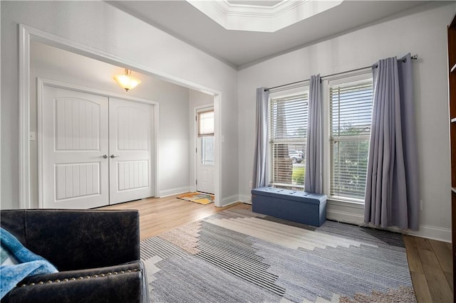 living area with crown molding, baseboards, a tray ceiling, and wood finished floors