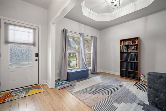 entrance foyer featuring a raised ceiling, ornamental molding, baseboards, and wood finished floors