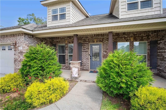entrance to property featuring covered porch, brick siding, a garage, and a shingled roof