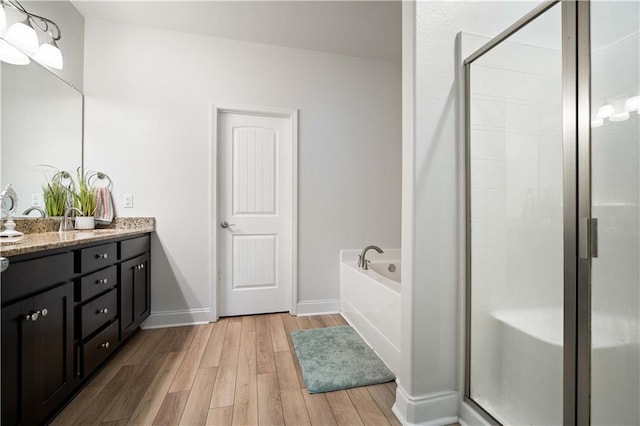 bathroom featuring a bath, a shower stall, baseboards, wood finished floors, and vanity