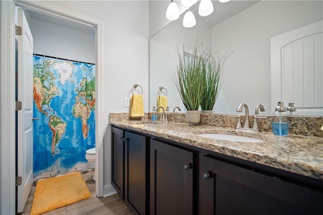 full bath with double vanity, a sink, toilet, and wood finished floors