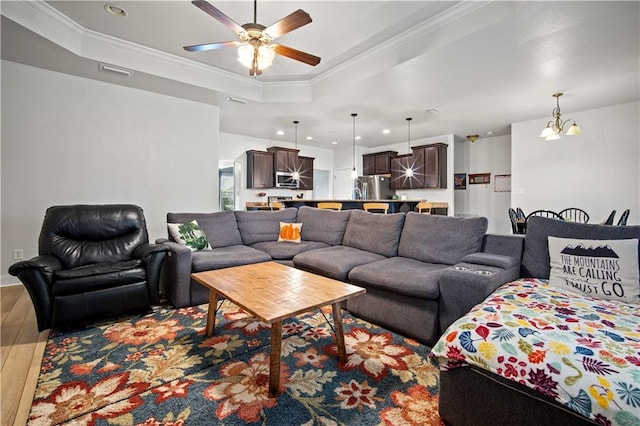 living room with ornamental molding, ceiling fan with notable chandelier, hardwood / wood-style flooring, and a tray ceiling