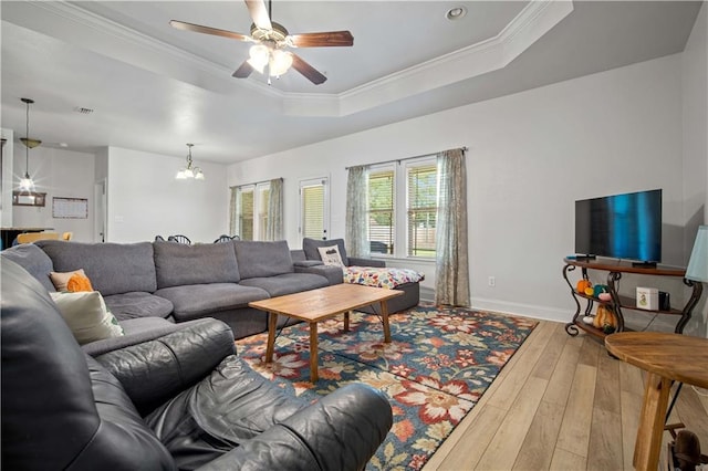 living room featuring hardwood / wood-style floors, ceiling fan with notable chandelier, a raised ceiling, and ornamental molding