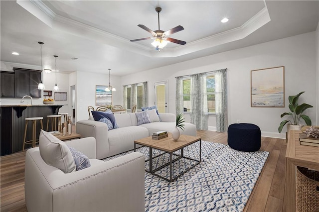 living room featuring crown molding, baseboards, a raised ceiling, hardwood / wood-style flooring, and a ceiling fan