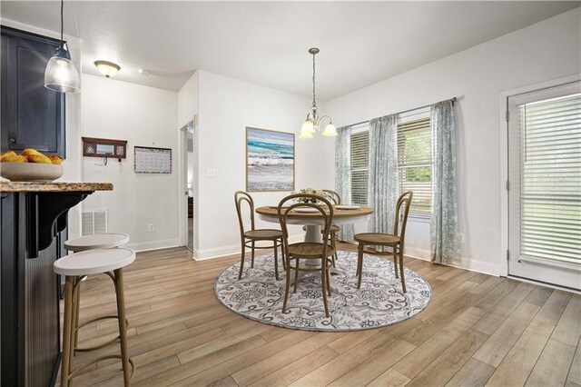 kitchen with sink, appliances with stainless steel finishes, light stone countertops, decorative light fixtures, and light wood-type flooring