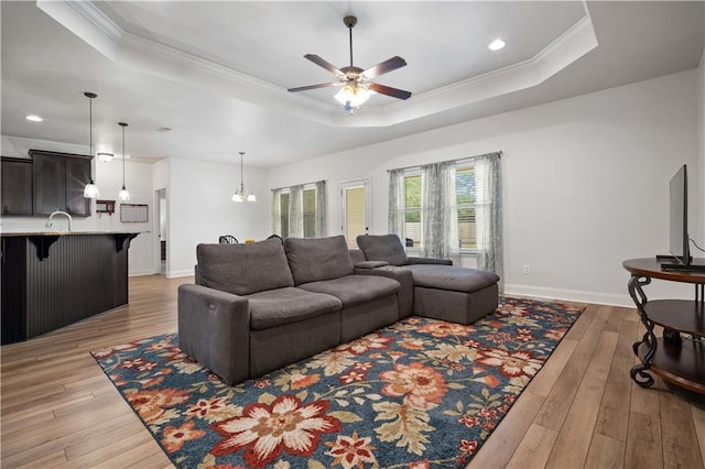 living room with light wood-style flooring, ornamental molding, baseboards, a raised ceiling, and a ceiling fan