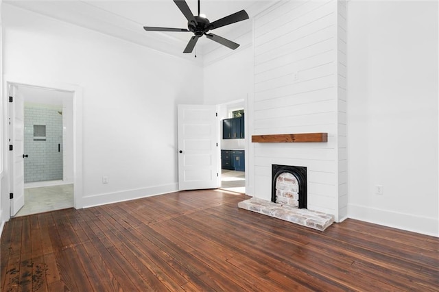 unfurnished living room with dark wood-type flooring, crown molding, a fireplace, a towering ceiling, and ceiling fan