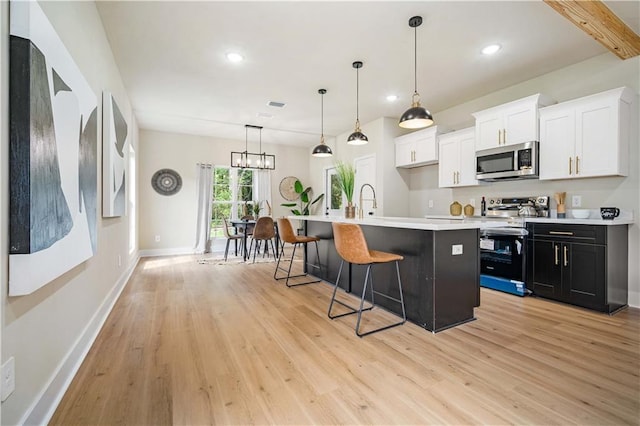 kitchen with hanging light fixtures, a center island with sink, light wood-type flooring, white cabinets, and appliances with stainless steel finishes