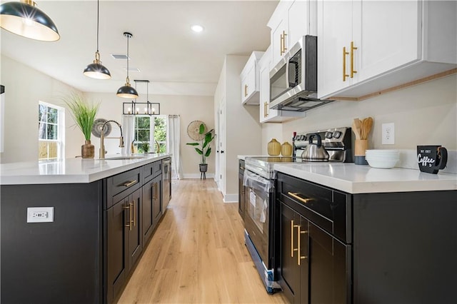 kitchen featuring decorative light fixtures, white cabinets, light hardwood / wood-style floors, electric stove, and a kitchen island with sink