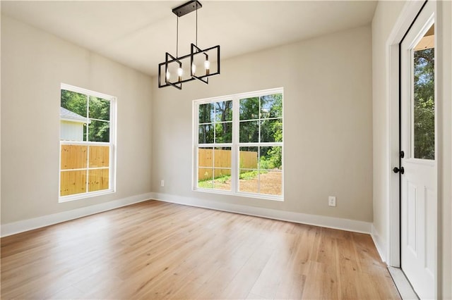 unfurnished dining area featuring light wood-type flooring, a healthy amount of sunlight, and a notable chandelier